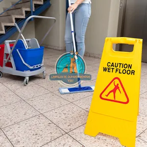 Operario trapeando el piso junto a una señal de piso mojado en una limpieza de final de obra